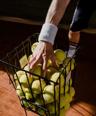 Person holding green tennis balls in black metal basket