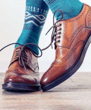 Classic brown men's brogues shoes and a man in blue socks. Men's stylish look.