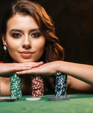 attractive brown haired girl leaning on poker chips and looking at camera isolated on black