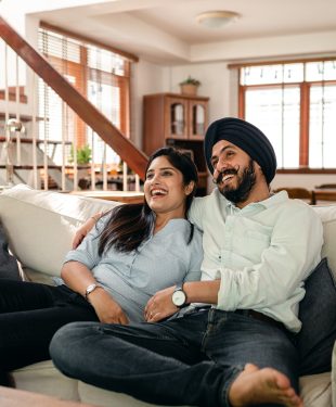 Joyful young indian couple cuddling while watching funny film on tv