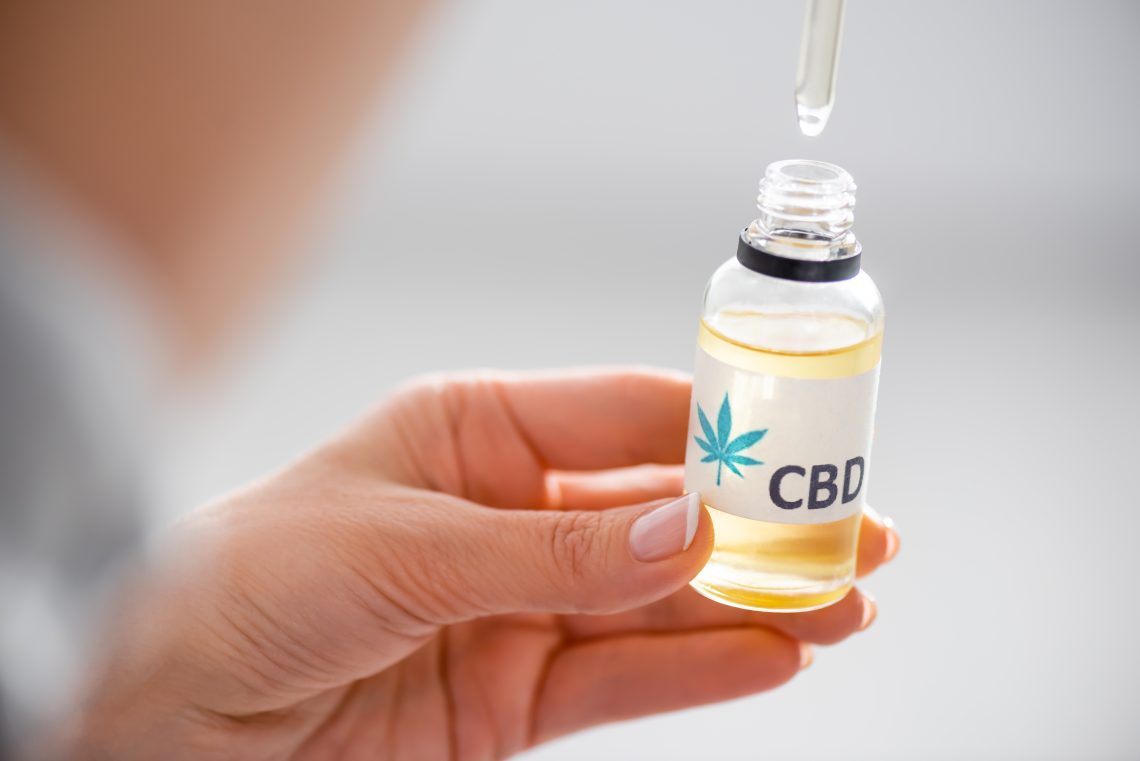 selective focus of woman holding pipette and bottle with cbd lettering